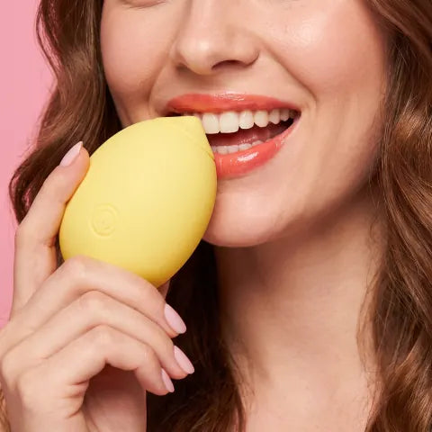 Smiling woman playfully biting the Limone against a pink background